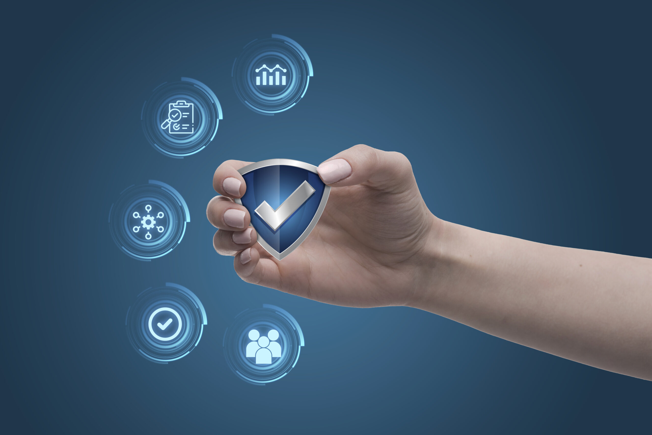 Uma mão segurando um ícone de escudo azul com uma marca de verificação, cercada por ícones digitais que representam dados, gráficos, rede e pessoas, em um fundo azul escuro.